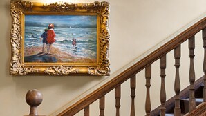 A staircase with a wooden handrail and a balustrade, leading to a landing with a framed painting of a beach scene. - The Ryebeck Country House & Restaurant (Windermere)