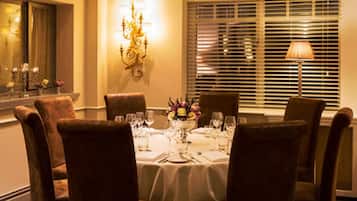 A dining room with a round table set for four, surrounded by brown upholstered chairs.