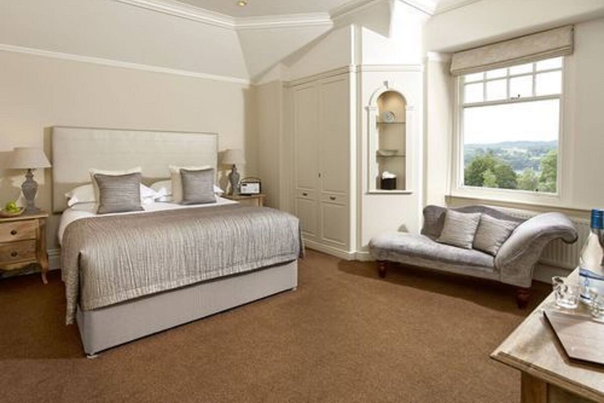 A bedroom with a large bed, a nightstand, a dresser, a window with a view, and a small table with a bottle and glasses.