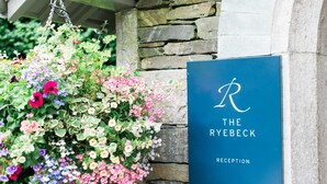 A reception sign with a large 'R' and the text 'THE RYEBECK' above 'RECEPTION' on a blue background, mounted on a stone wall.