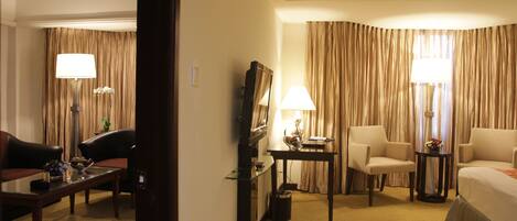 A hotel room with a bed, two armchairs, a desk, a lamp, and curtains.
