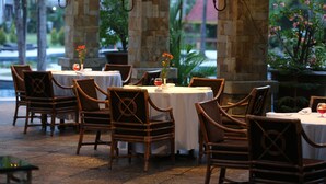 An outdoor dining area with round tables and wicker chairs, stone pillars, and ambient lighting. - Aryaduta Pekanbaru (Pekanbaru)