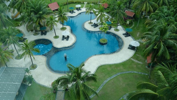 An aerial view of a resort with a central swimming pool, surrounded by palm trees and lounge areas. - Aryaduta Pekanbaru (Pekanbaru)