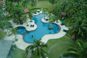 Vista aérea de un resort con piscina central, rodeado de palmeras y zonas de descanso.