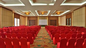 A conference room with rows of red chairs, a patterned carpet, and a large screen at the front.