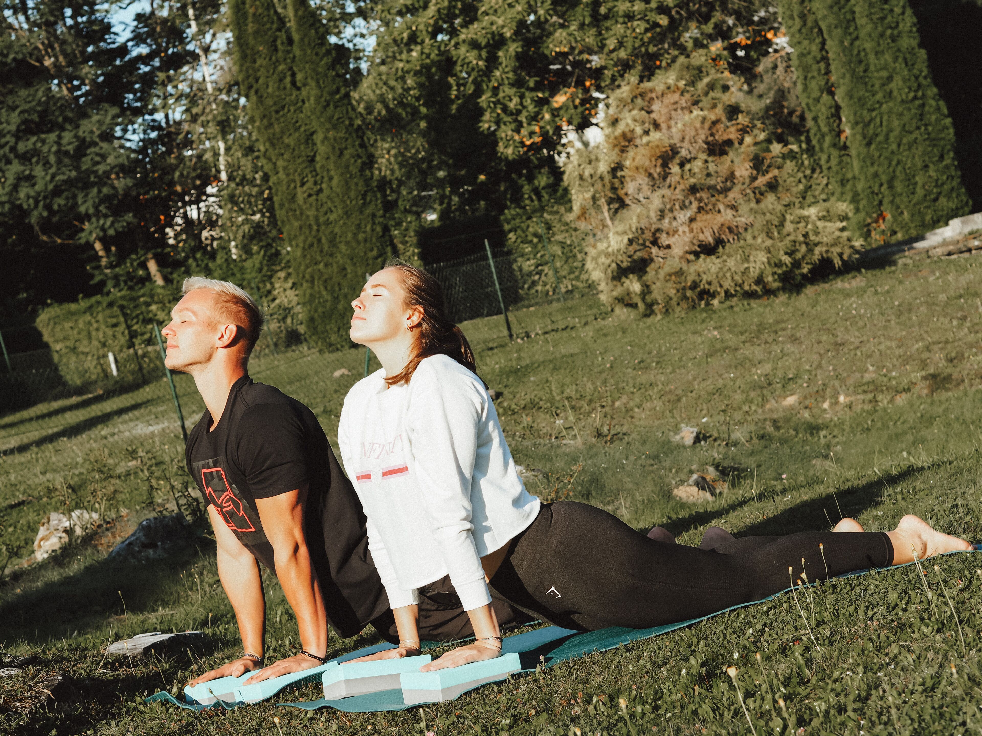 Two people doing yoga on a grassy field with trees in the background.