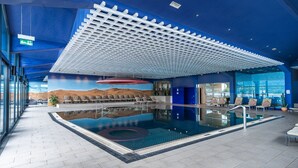 A modern indoor pool area with a ceiling design, a pool with a hot tub, and a desert-themed mural.