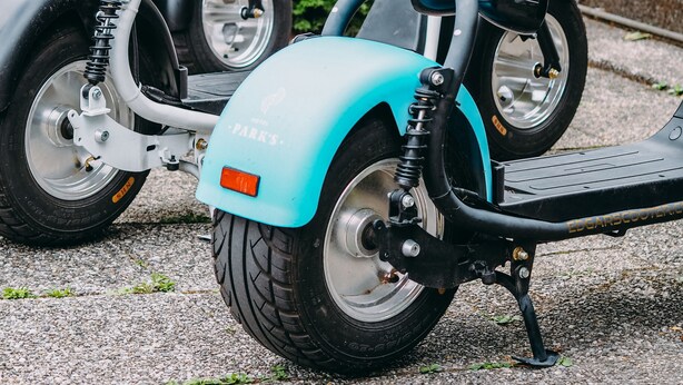 Two electric scooters parked on a gravel surface with greenery in the background. - Hotel Parks (Velden am Wörther See)