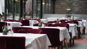 A restaurant with tables set for dining, featuring red velvet chairs and white tablecloths.
