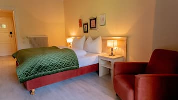 Een hotelkamer met een bed, nachtkastjes, een rode fauteuil en een radiator.