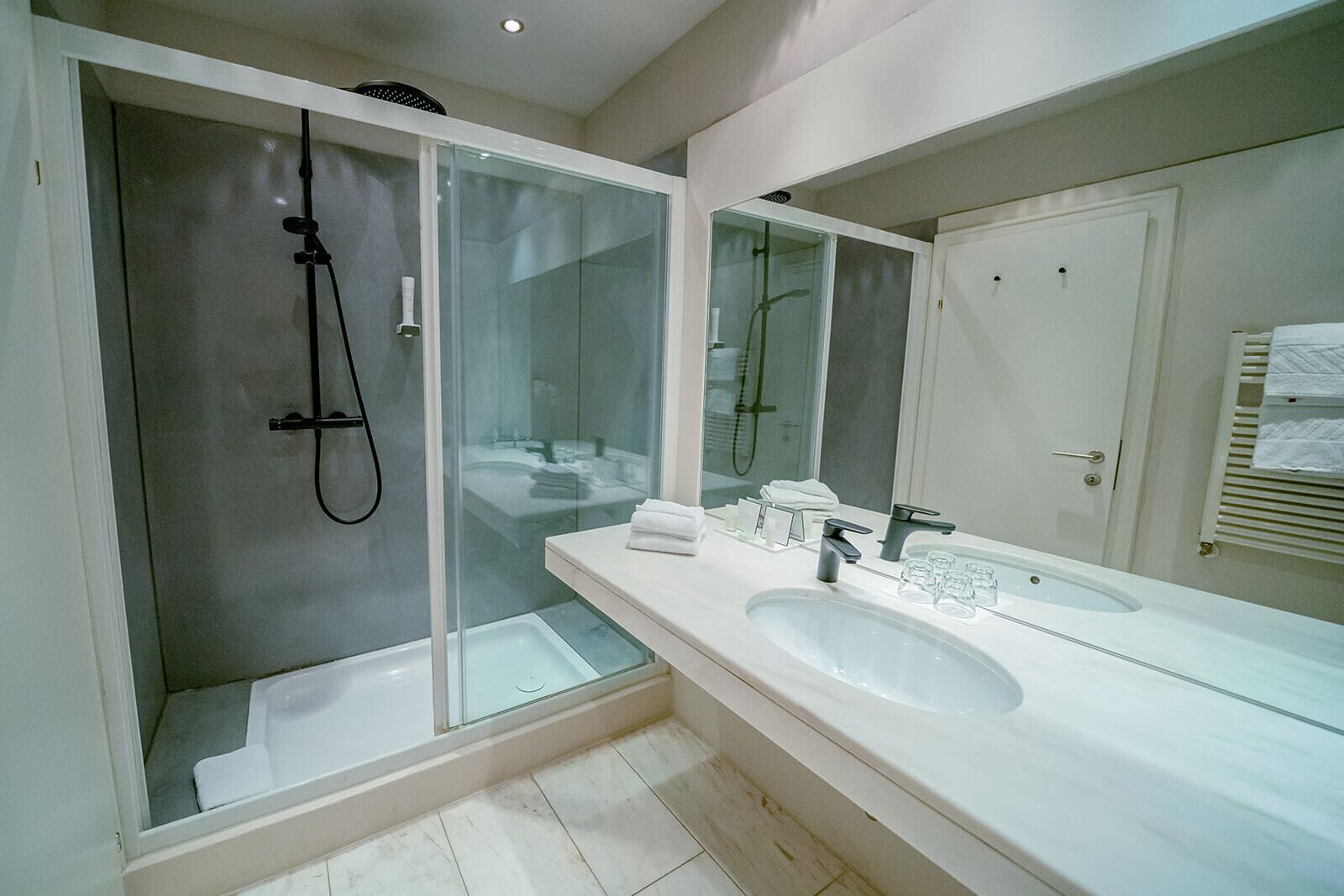 Une salle de bain moderne avec une douche à parois de verre, un grand miroir et un meuble-lavabo blanc.
