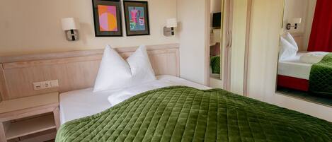A hotel room with a bed, a bedside table, a mirror, and two wall-mounted picture frames.
