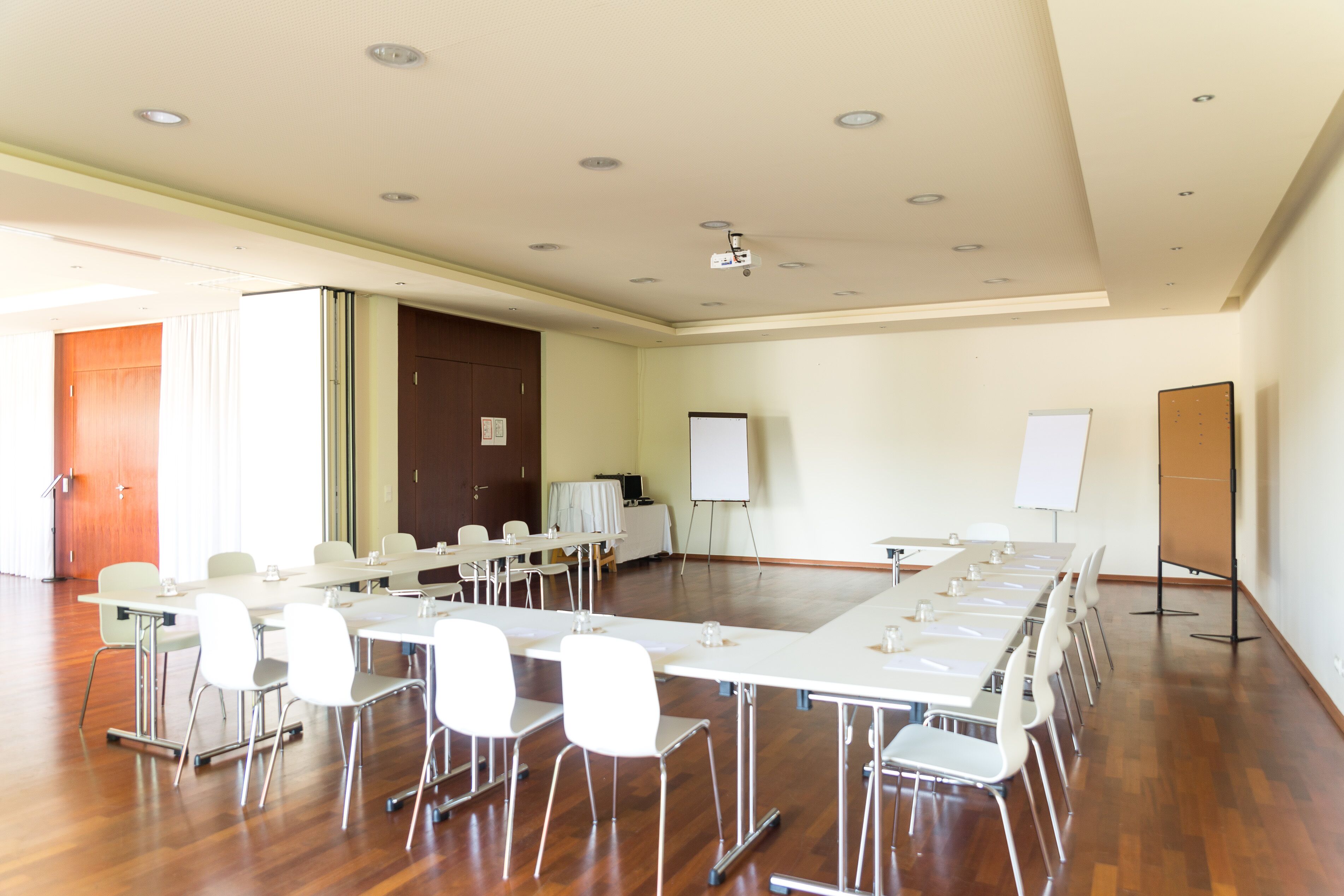 Una sala conferenze con un lungo tavolo, sedie bianche, una lavagna e un proiettore.