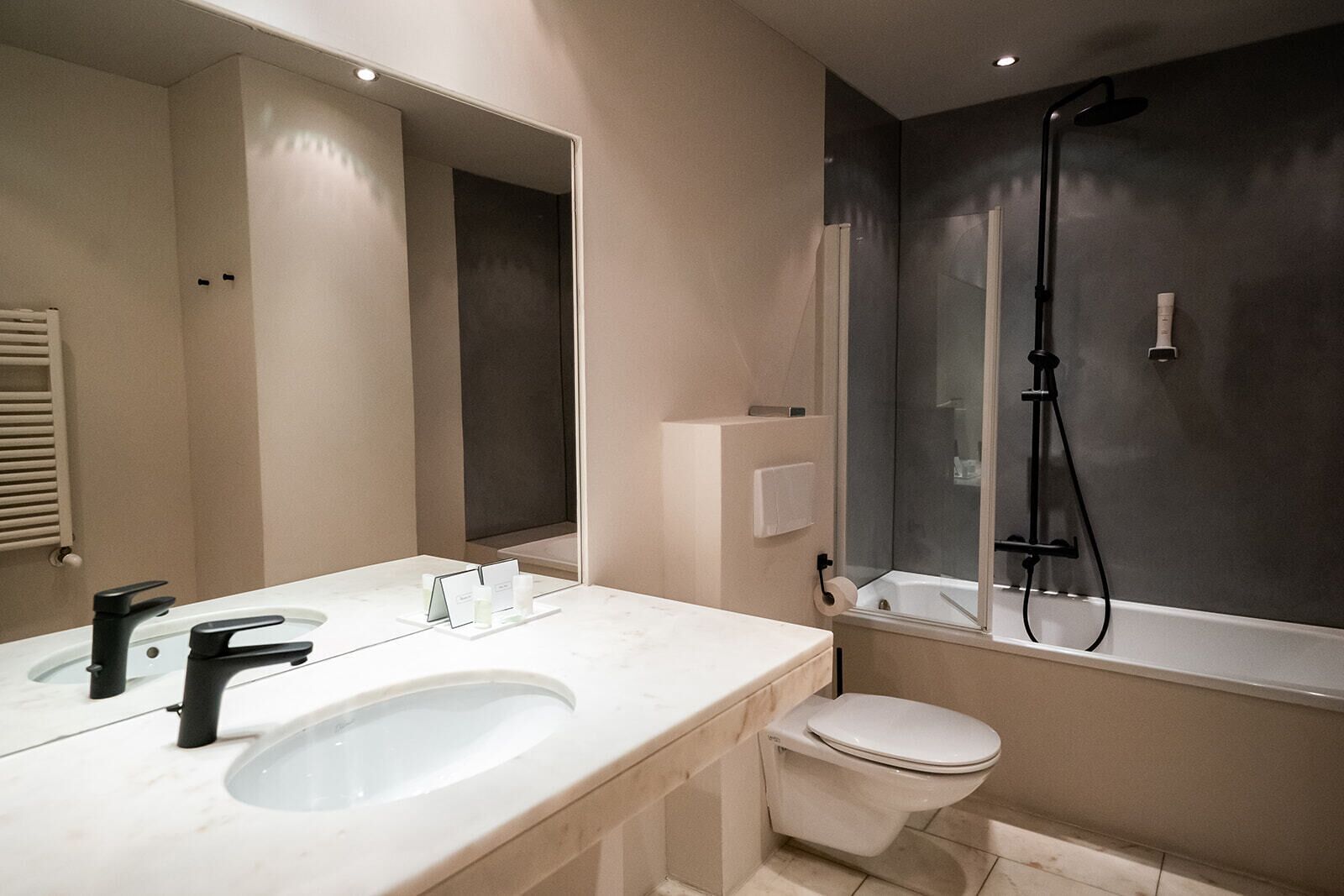 Ein modernes Badezimmer mit einem weißen Waschbecken, einem schwarzen Wasserhahn und einer Duschkabine aus Glas.