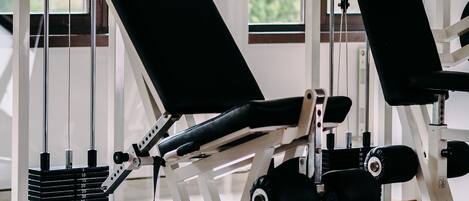 Un gimnasio con máquinas de pesas, colchonetas de ejercicio y un ventanal con vistas a zonas verdes.