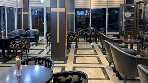 Un restaurante moderno con mesas redondas y sillas estampadas, suelo de baldosas y vistas al exterior a través de amplios ventanales.