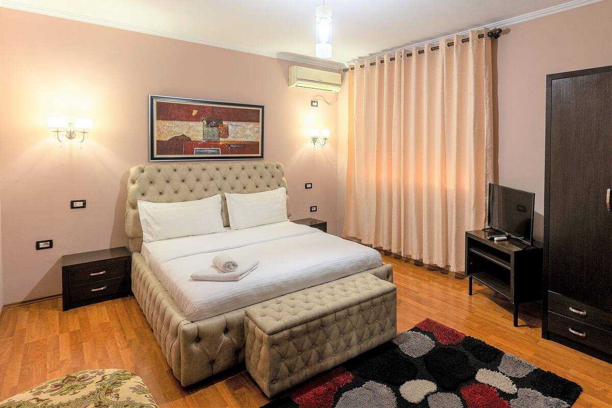 Un dormitorio con una cama grande, una mesita de noche, un mueble para la televisión y un armario.