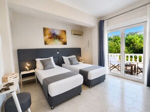 A hotel room with two beds, a desk, and a balcony with a view of greenery. - Villa Small Paradise (Rhodes)