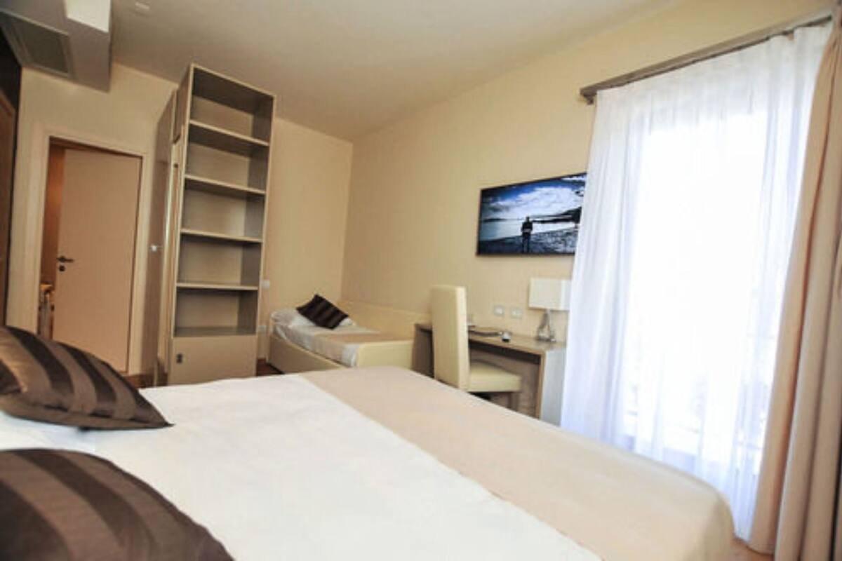 A hotel room with a bed, a desk, a chair, a wardrobe, and a painting on the wall.
