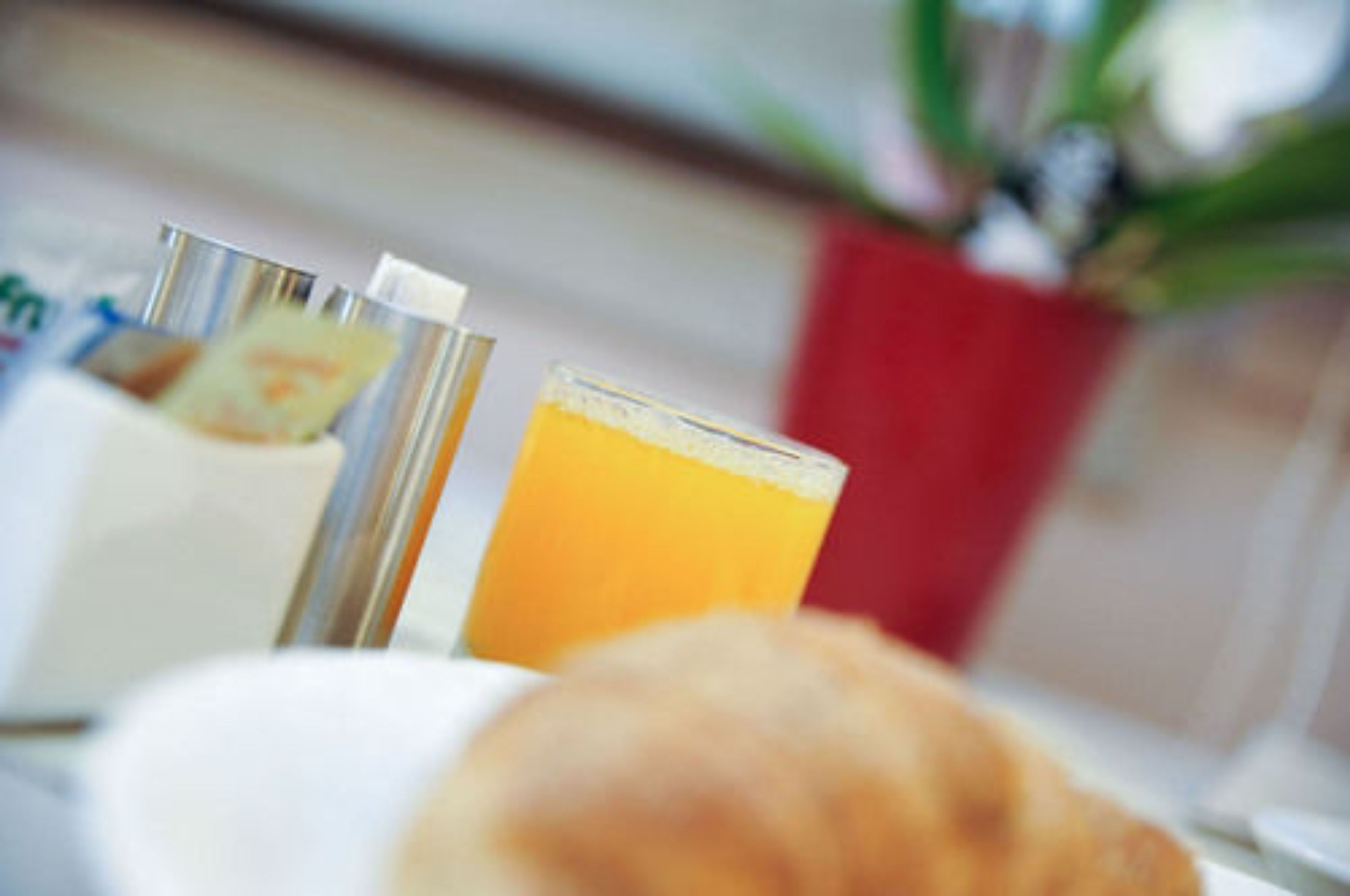 A breakfast setting with a croissant, a glass of orange juice, and a red vase with flowers.