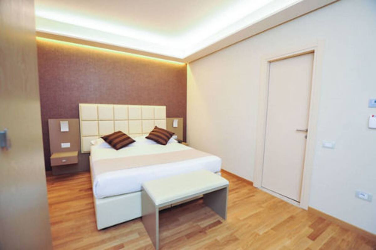 A modern bedroom with a large bed, bedside tables, a bench, and a door.