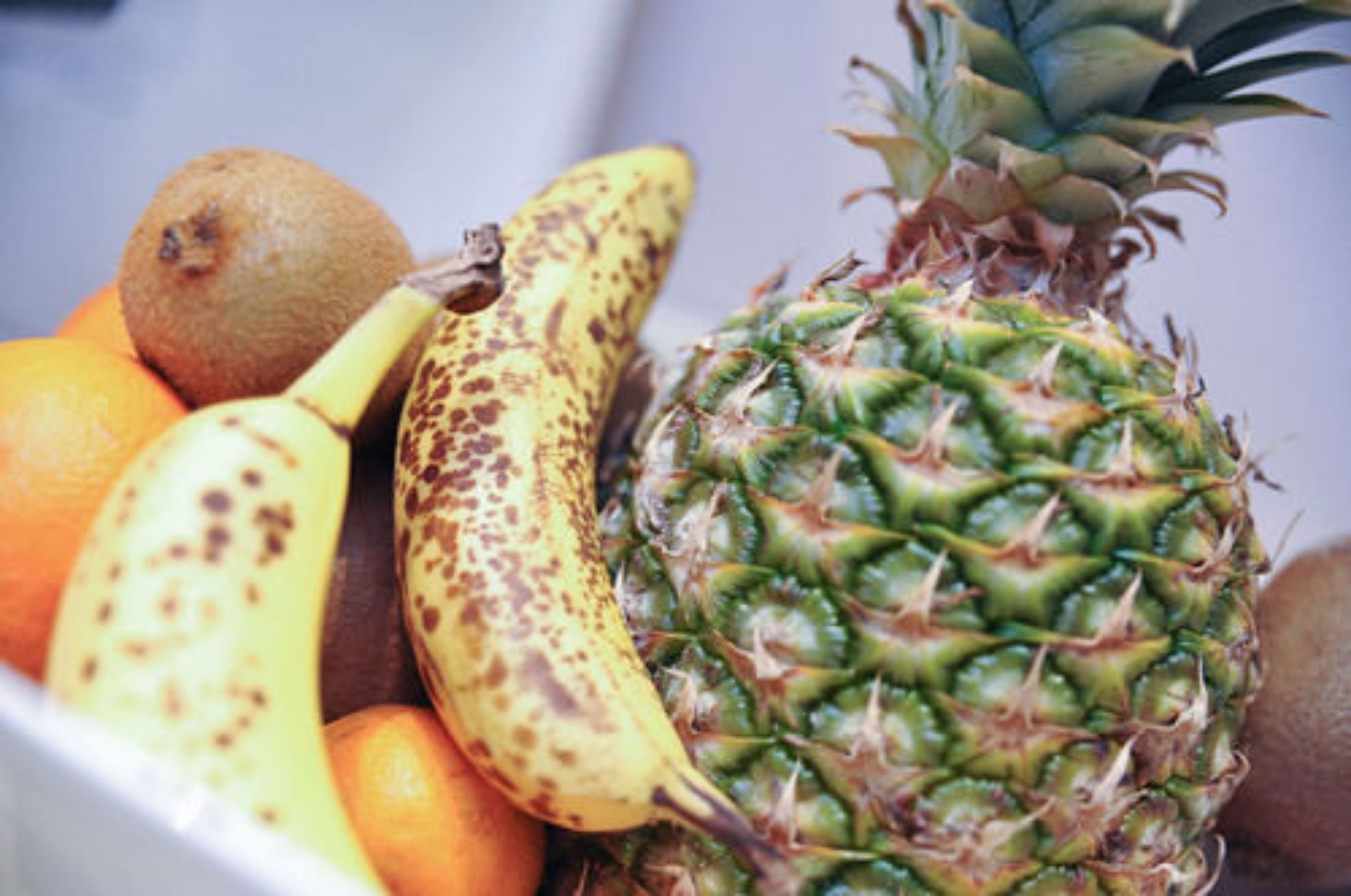 Un tazón con una banana, piña y naranjas.