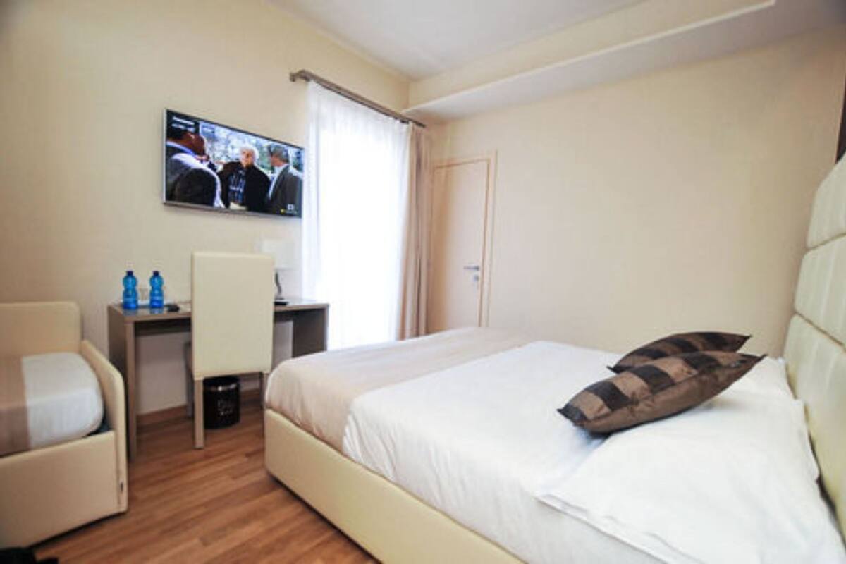 A hotel room with a bed, a desk, a chair, a television, and a door.