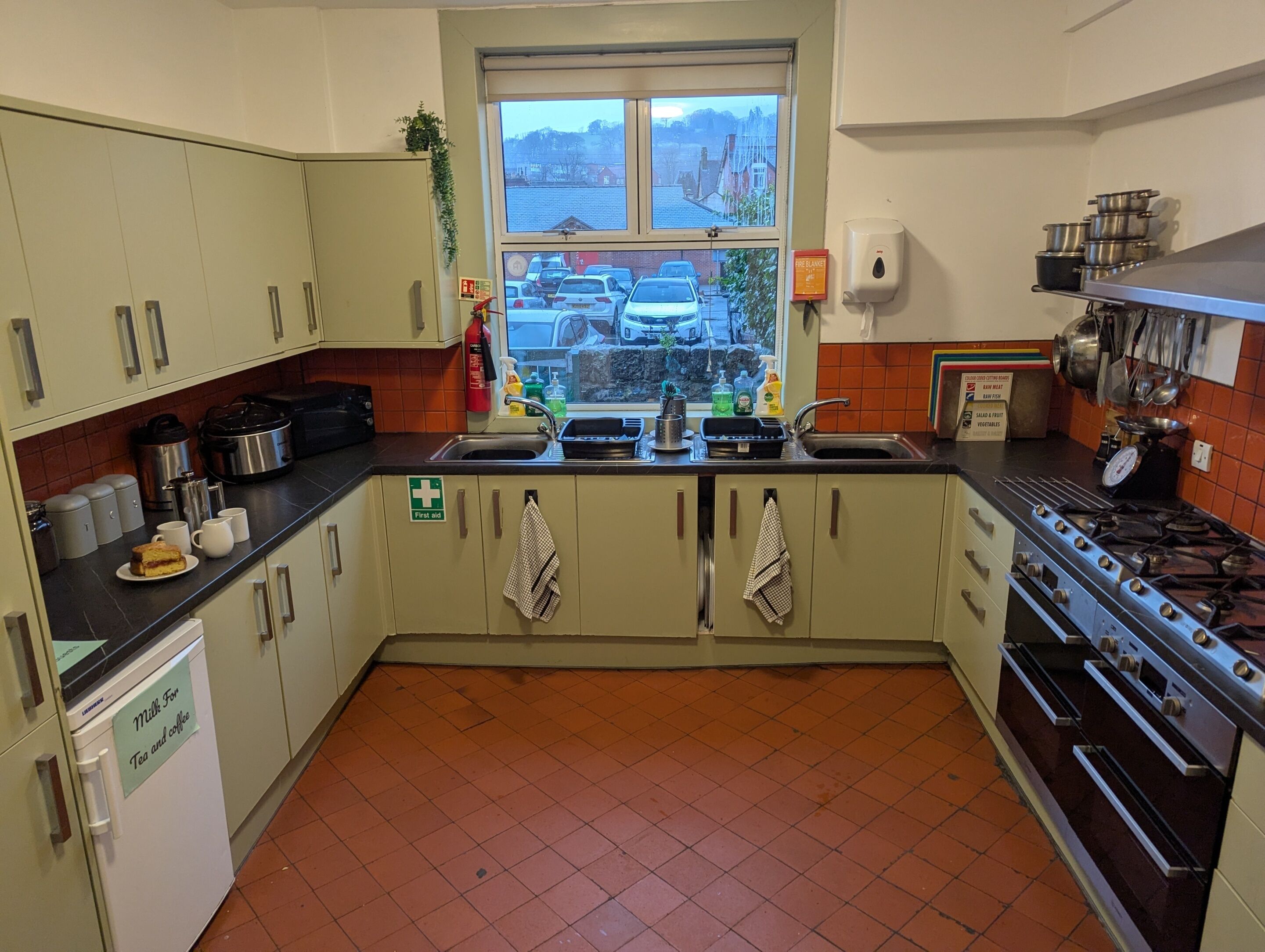 A compact kitchen with a window view, a sink, a stove, and a milk dispenser.
