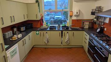 A compact kitchen with a window view, a sink, a stove, and a milk dispenser.