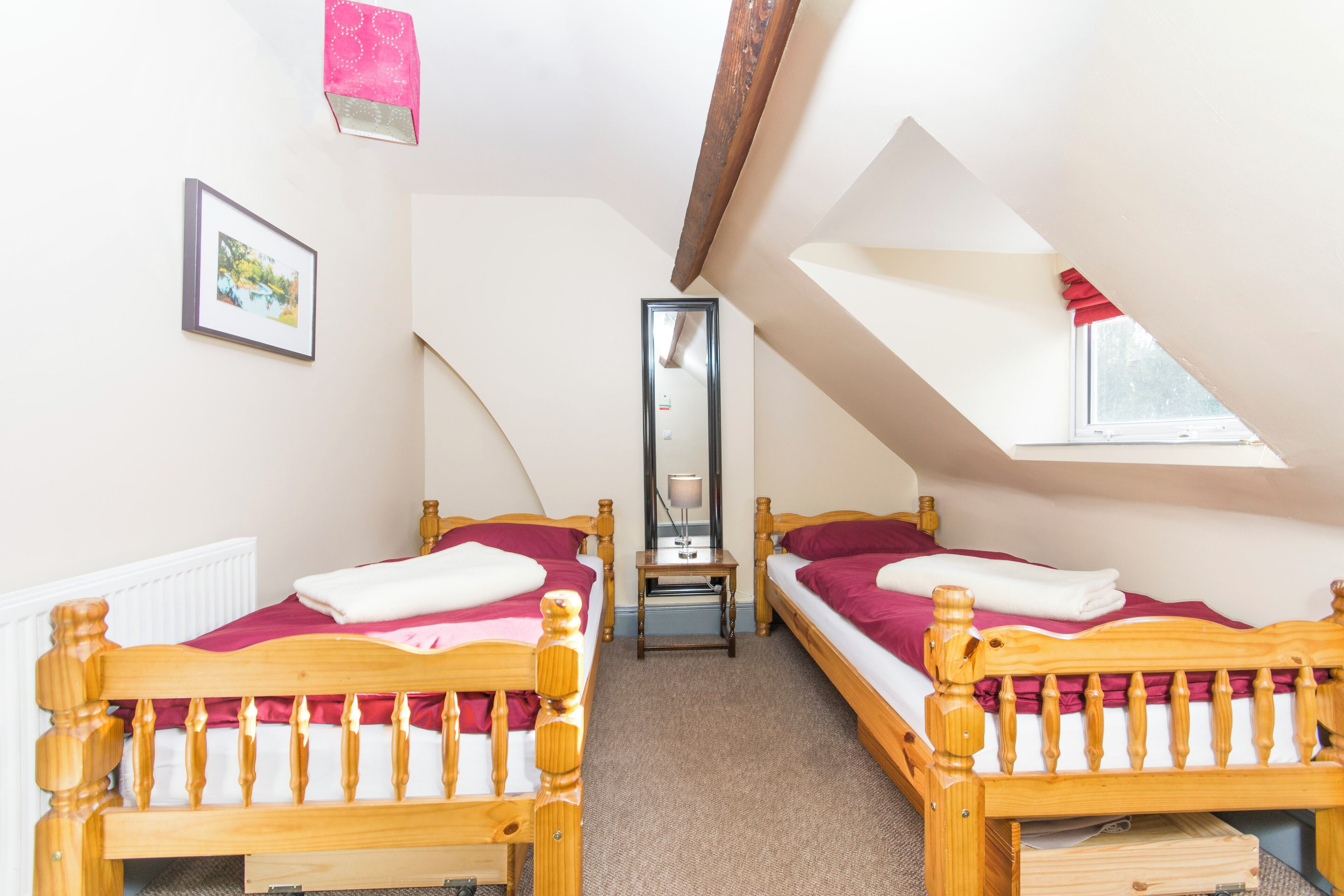 A room with two wooden beds, a mirror, and a window.