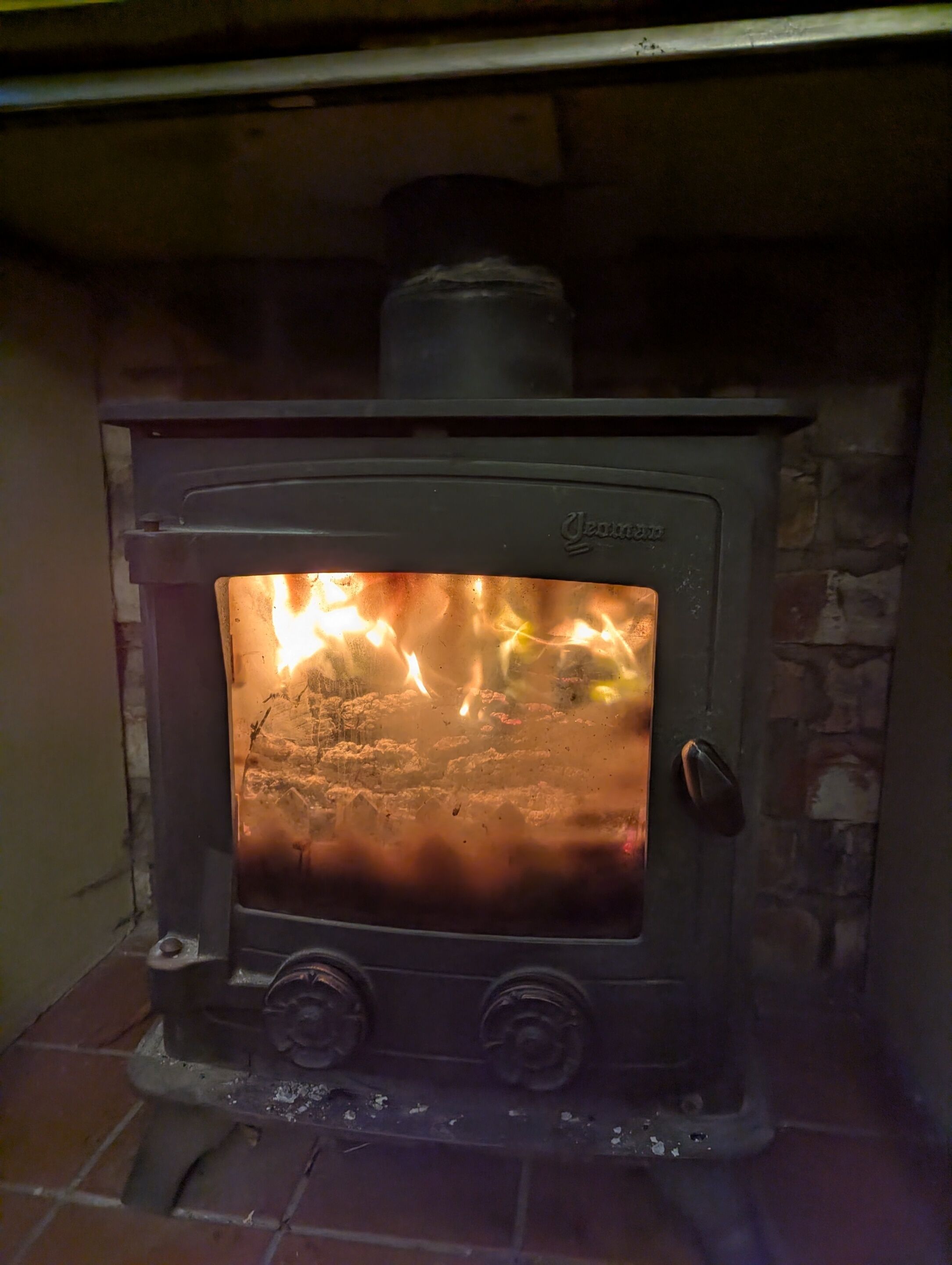En vedeldad kamin med synliga lågor inuti, en kontrollpanel med två vred och en skorsten på ovansidan.