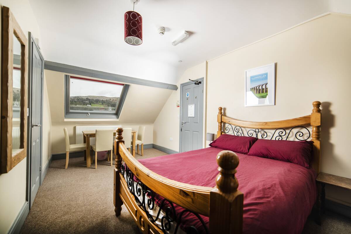 A bedroom with a large bed, a desk, and a window overlooking a landscape.