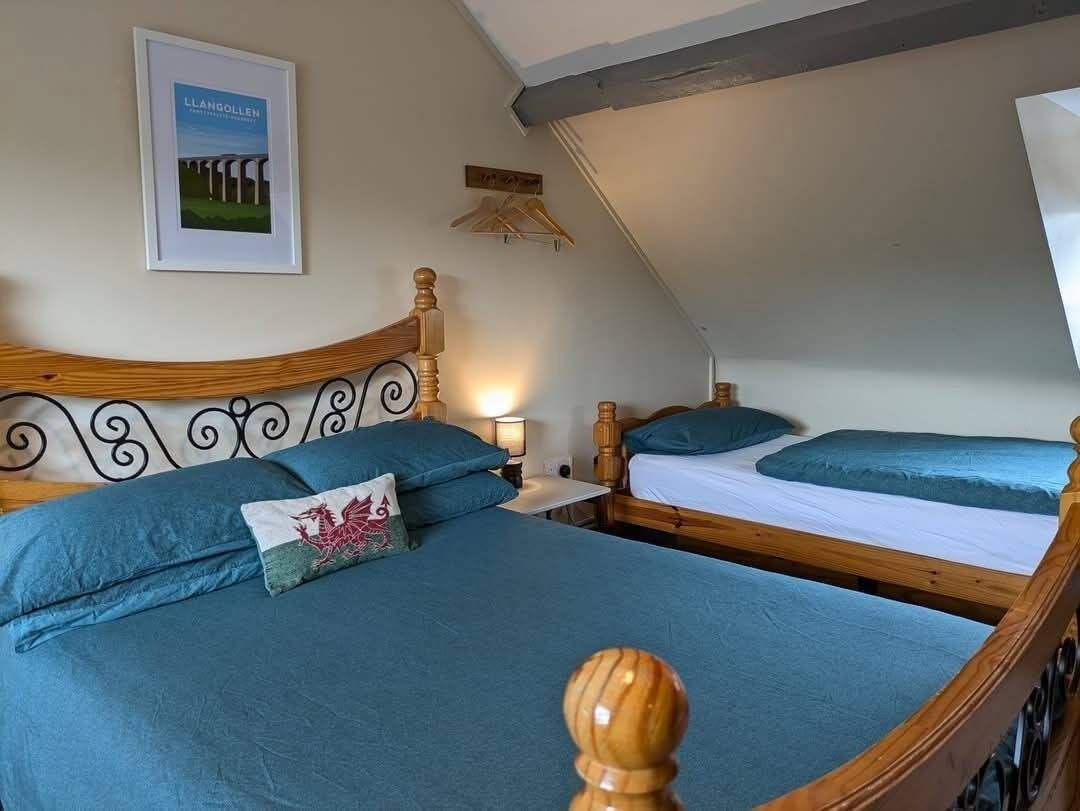 A bedroom with two beds, each with a wooden headboard and blue bedding. There is a framed picture on the wall and a wooden hanger on the wall.