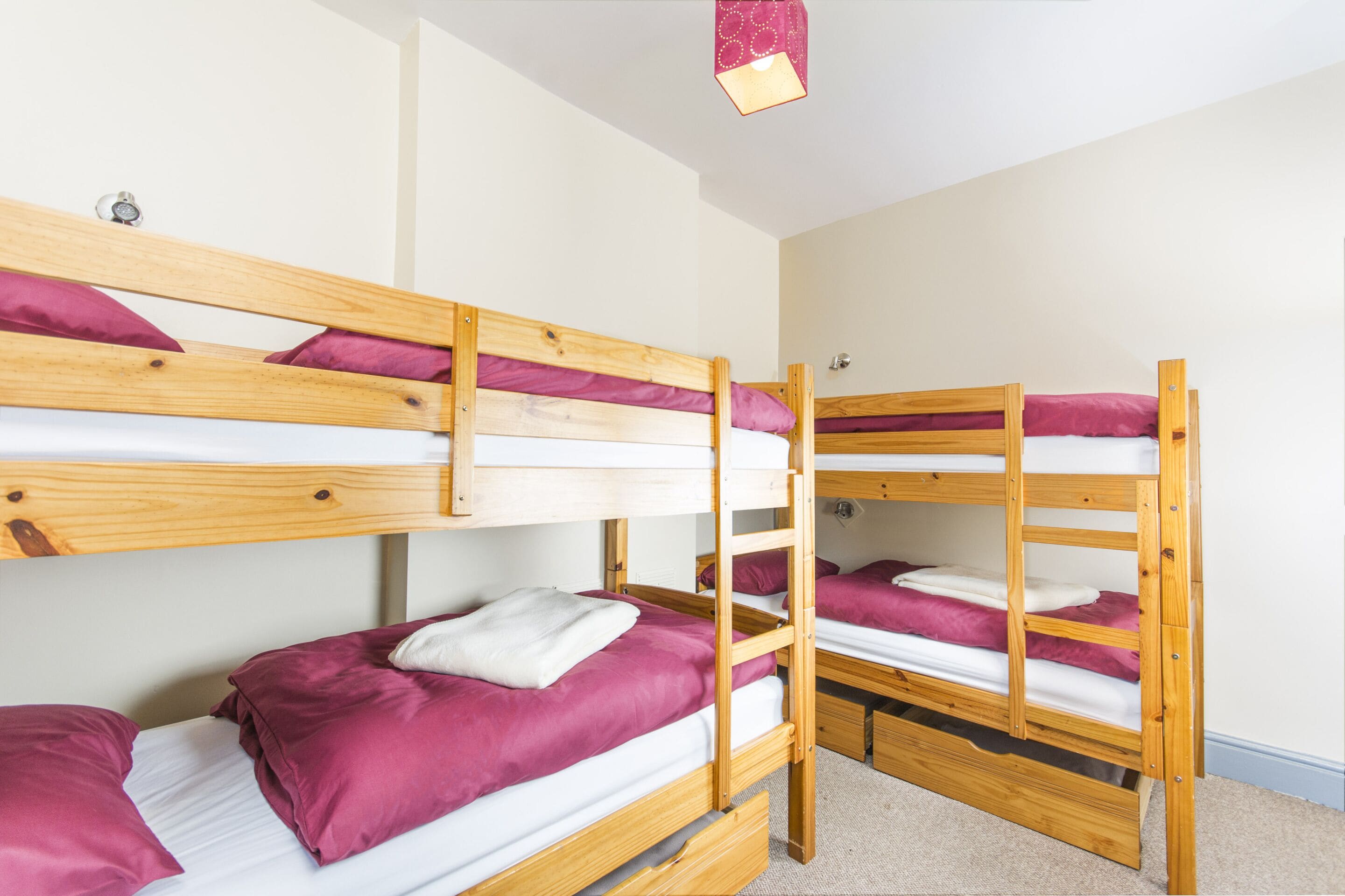 A bunk bed room with wooden frames, white bedding, and pink pillows.