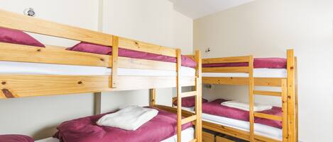 A bunk bed room with wooden frames, white bedding, and pink pillows.