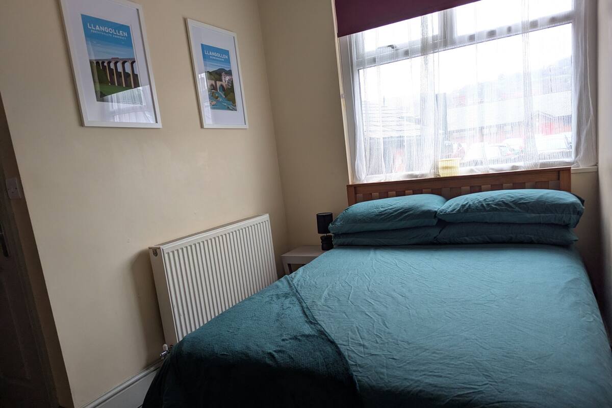 A bedroom with a bed, a radiator, and two framed pictures on the wall.