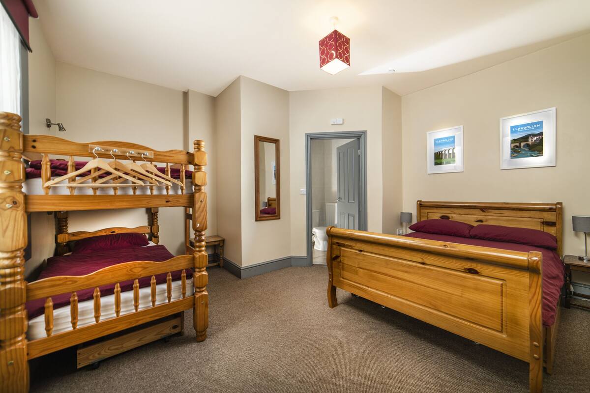 A bedroom with two wooden bunk beds, a bedside table, a mirror, and two framed pictures on the wall.