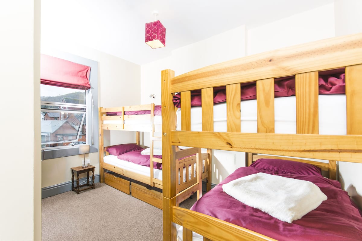 A room with three bunk beds, a small table, and a window with a view of buildings.