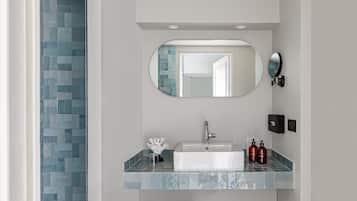 A bathroom with a tiled wall, a sink, a mirror, and two red bottles.