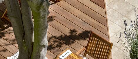 An outdoor wooden deck with a table and chairs, surrounded by white pebbles and a large tree.