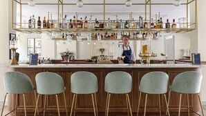 Zona de bar con un cantinero, taburetes y una estantería bien surtida con botellas y vasos.