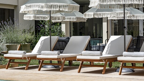 Un área junto a la piscina con sillones de descanso y sombrillas.