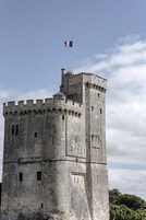 Una torre de piedra histórica con almenas, un asta de bandera y una bandera.