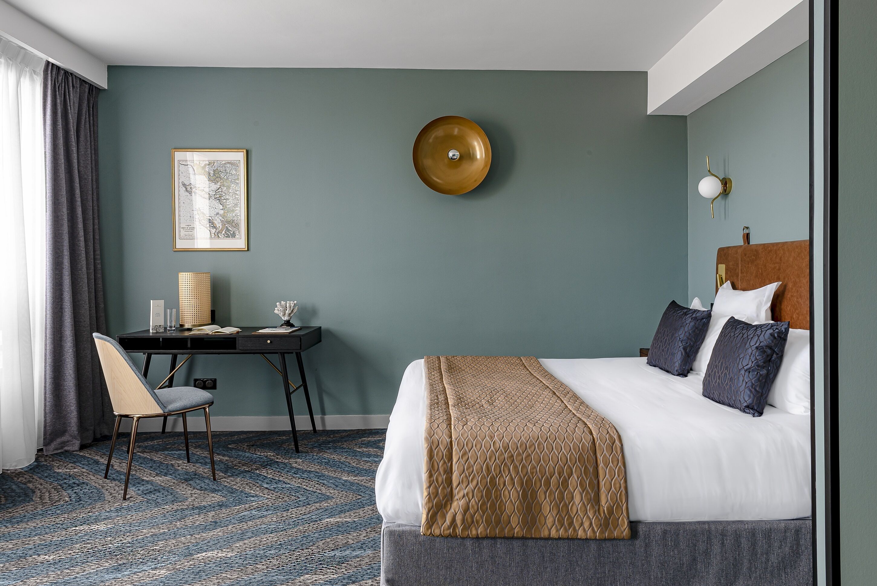 Une chambre d’hôtel avec un lit, un bureau, une chaise, une carte accrochée au mur et une lampe.