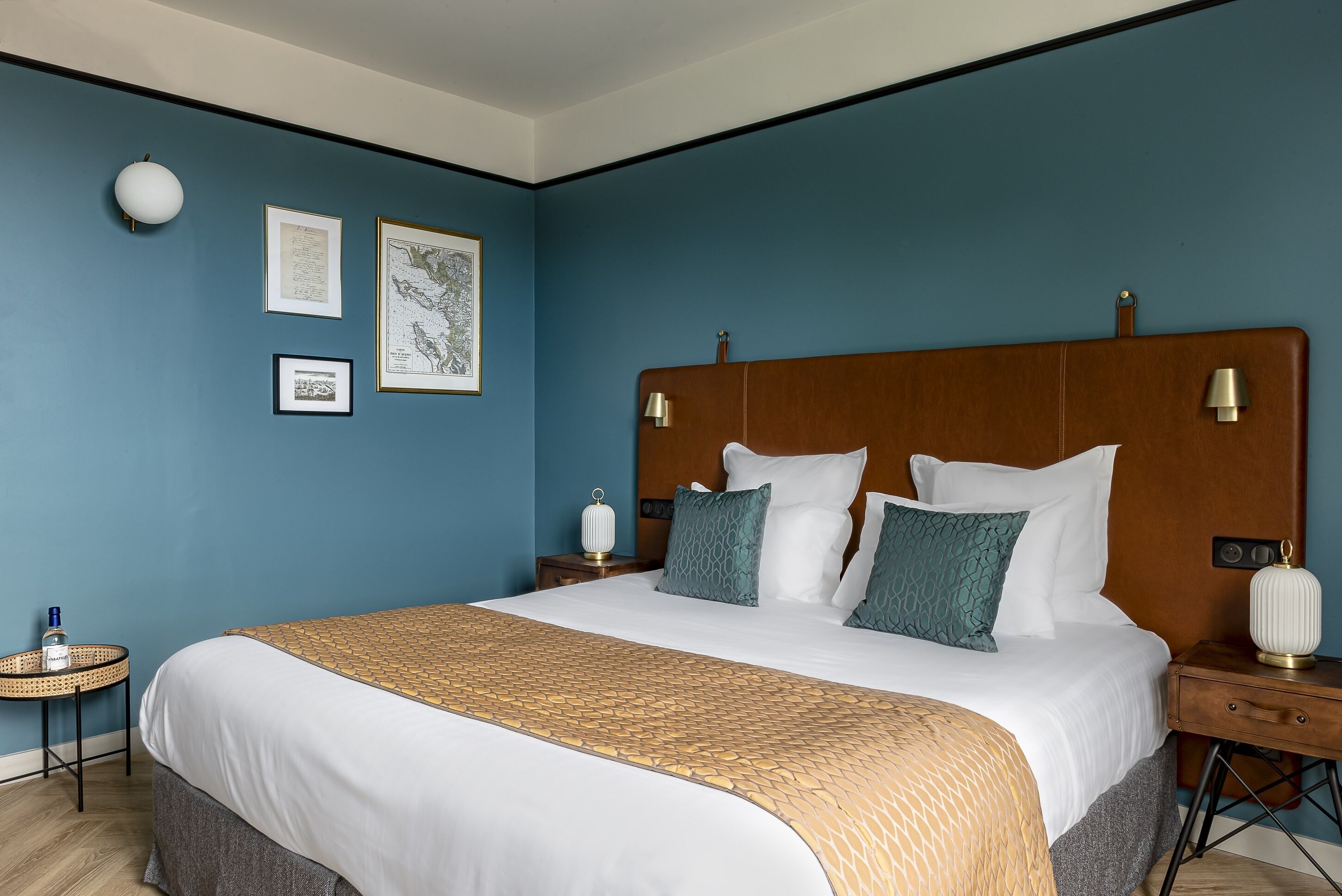 A neatly made bed with a wooden headboard, a bedside table with a lamp, and framed pictures on the wall.