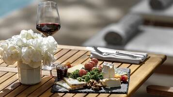 A wooden table with a cheese board, grapes, a glass of red wine, and a vase of white flowers.