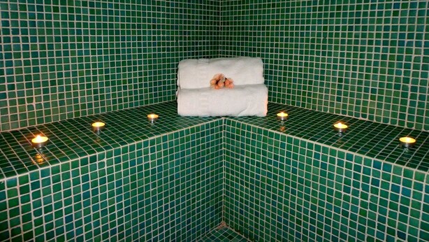A corner of a room with green mosaic tiles, a white towel, and three lit candles on the floor. - Alda Soria Rooms (Soria)