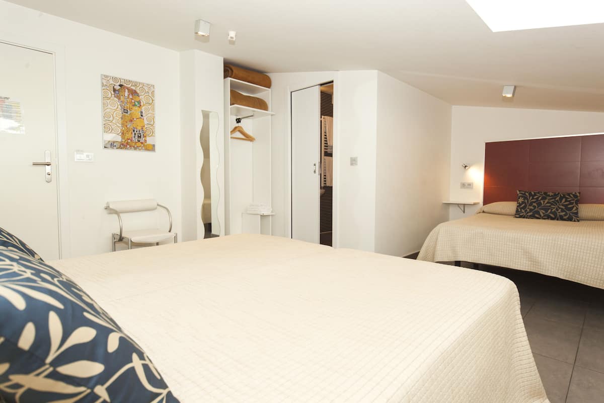 Habitación de hotel con una cama grande, una cama más pequeña, un vestidor, una silla y una obra de arte en la pared.