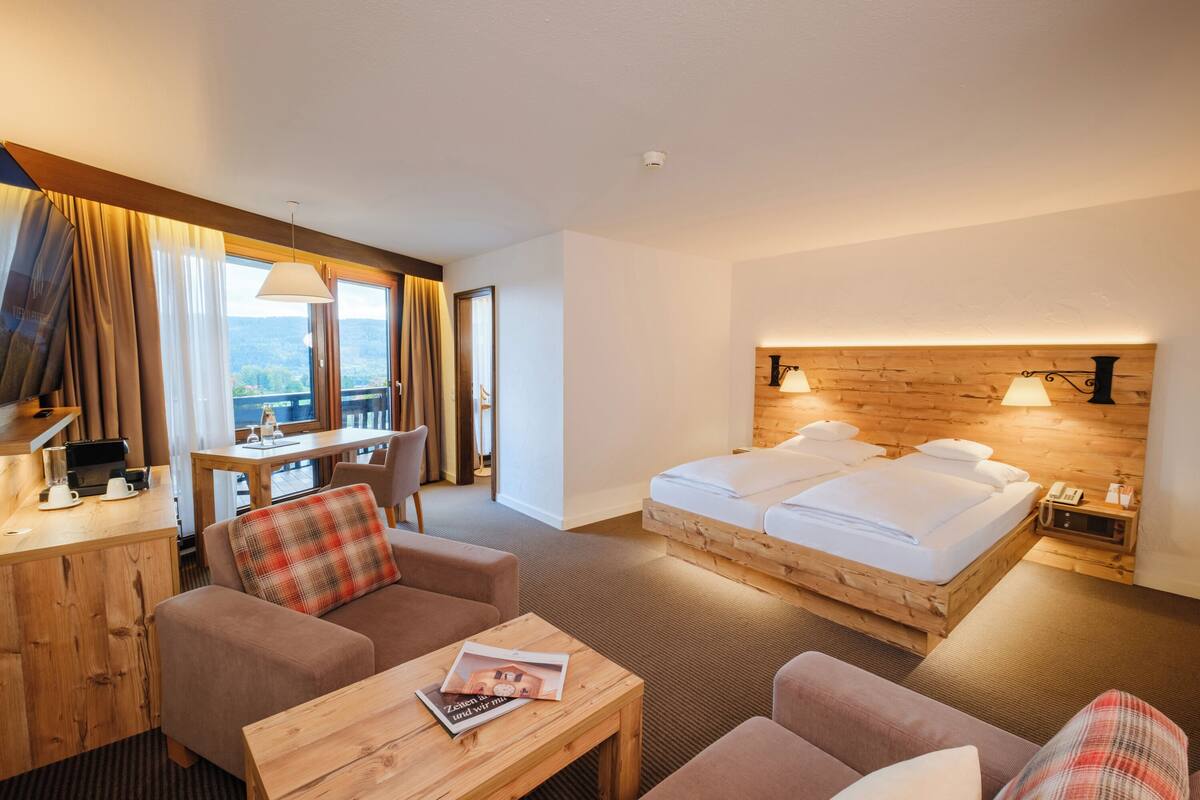 A hotel room with a wooden bed, a desk, a sofa, and a view of the outdoors.