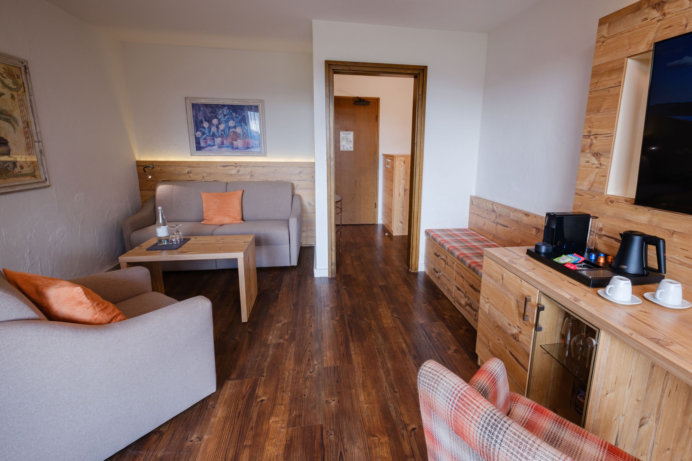 A modern living room with a sofa, a coffee table, a wooden cabinet with a television, and a wooden floor.